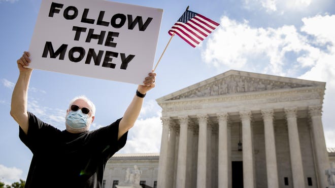 Bill Christeson sostiene un cartel que dice "Siga el dinero" frente a la Corte Suprema, el jueves 9 de julio de 2020, en Washington. La Corte Suprema dictaminó el jueves que el fiscal de distrito de Manhattan puede obtener declaraciones de impuestos de Trump.