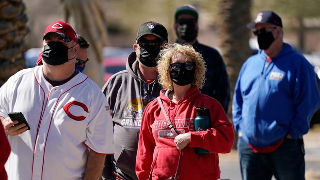 Baseball fans wait in line for the gates to open at Goodyear Ballpark prior to a spring training baseball game between the Cleveland Indians and the Cincinnati Reds on Sunday, Feb. 28, 2021, in Goodyear, Ariz.
