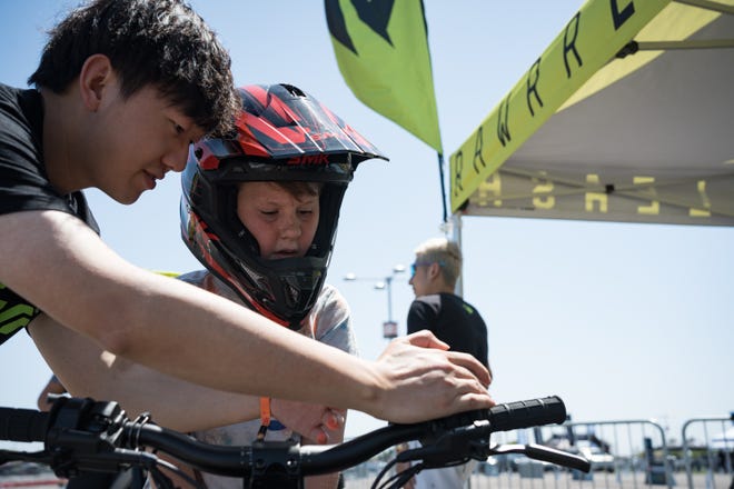 Justin Zheng teaches 9-year-old Levi Carmichael to drive the Rawrr Mantis Mini electric bike for kids at the Electrify Expo outside State Farm Stadium on May 4, 2024 in Glendale, Ariz.