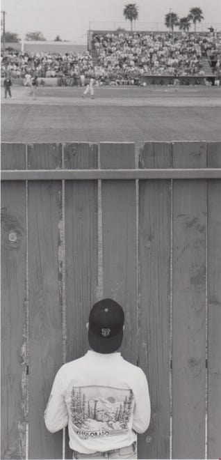 Arizona State University student Brian Hawkins, who is from the San Francisco Bay area, watches the Giants play the Cubs during spring training outside of Scottsdale Stadium March 14, 1991. The game was sold out so the Giants fan had to watch the game through wooden boards in left field.