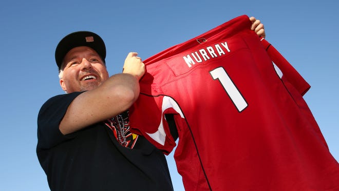Eric Polansky of Cave Creek, Ariz.,holds-up a Murray jersey after the Arizona Cardinals used their number one draft pick to select quarterback Kyler Murray from Oklahoma during the NFL Draft watch party at State Farm Stadium. | 2019 NFL draft | Cardinals draft Kyler Murray |