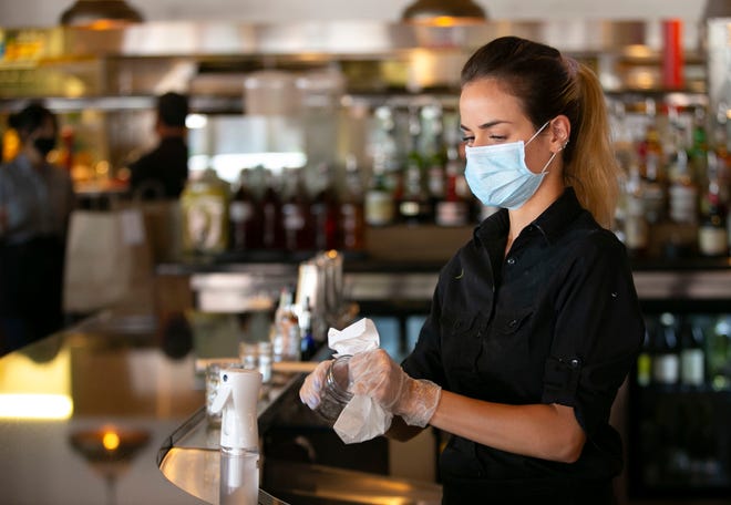Rafaila Mladjenovic, bartender del Macintosh, usa un spray desinfectante en un vaso cuando el d í a en que el restaurante en Phoenix reabre por primera desde mediados de marzo, el 11 de mayo de 2020. Se permiti ó a los restaurantes de todo el estado reabrir para ofrecer comida en el lugar siguiendo ciertas pautas.