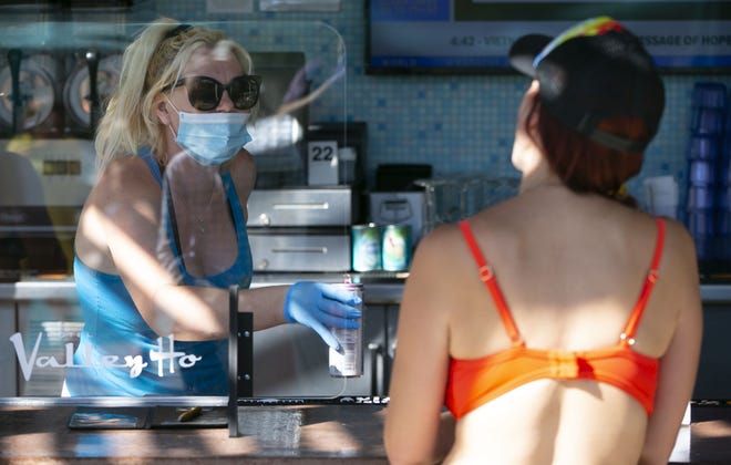 Karissa Lameyer, a server at the Hotel Valley Ho, serves a drink to a guest at the pool bar at the Hotel Valley Ho in Scottsdale on May 22, 2020. With demand starting to pick back up at the Hotel Valley Ho, the hotel has implemented procedures such as partitions, limiting capacity and having staff wear masks during the COVID-19 pandemic.