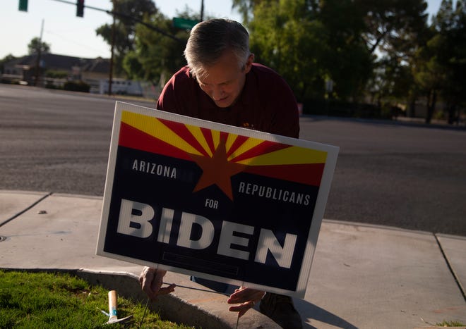 Un hombre coloca un cartel de Joe Biden en el cesped.