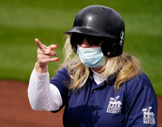 A security works wears a batting helmet and a mask during the spring training opener as the Colorado Rockies host the Arizona Diamondbacks at Salt River Fields at Talking Stick in Scottsdale, Ariz., on Feb. 28, 2021.