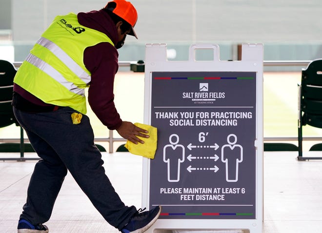 A worker cleans a social distancing sign during the Arizona Diamondbacks spring training opener against the Colorado Rockies at Salt River Fields at Talking Stick in Scottsdale, Ariz., on Feb. 28, 2021.