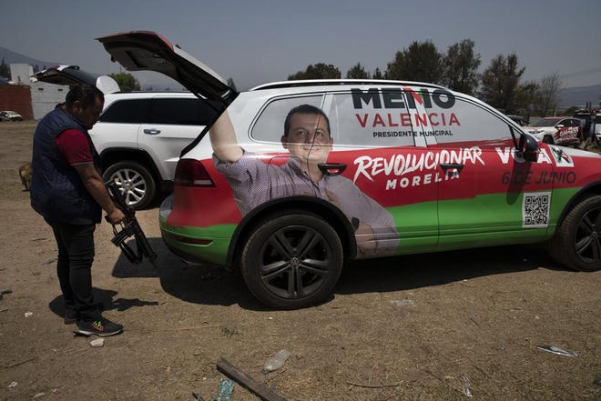 Un guardaespaldas y chofer de Guillermo Valencia, candidato a alcalde de la ciudad de Morelia por el Partido Revolucionario Institucional, toma su fusil de asalto de la parte trasera de la camioneta blindada en la que viajan, durante una escala de campaña de Valencia el sábado 22 de mayo de 2021 en Morelia, estado de Michoacán, México.