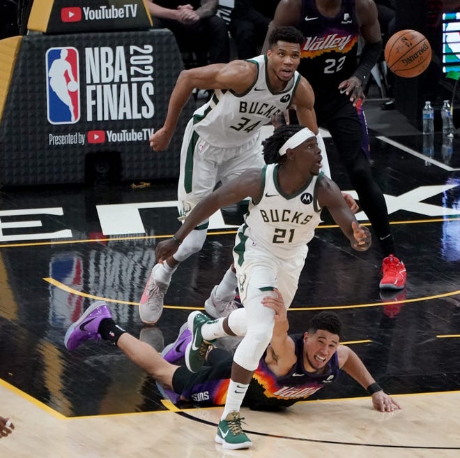 Milwaukee Bucks guard Jrue Holiday (21) keeps his eye on the ball after recovering it from Phoenix Suns guard Devin Booker (1) on the floor during the fourth quarter of Game 5 of Bucks 123-119 win over the Phoenix Suns in the NBA Finals at Footprint Center in Phoenix on Saturday.