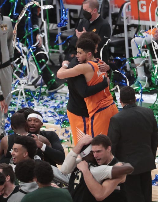 Phoenix Suns' Cameron Johnson (23) and Devin Booker (1) hug as Milwaukee Bucks players celebrate after winning Game 6 of the NBA Finals against the Phoenix Suns at Fiserv Forum July 20, 2021.