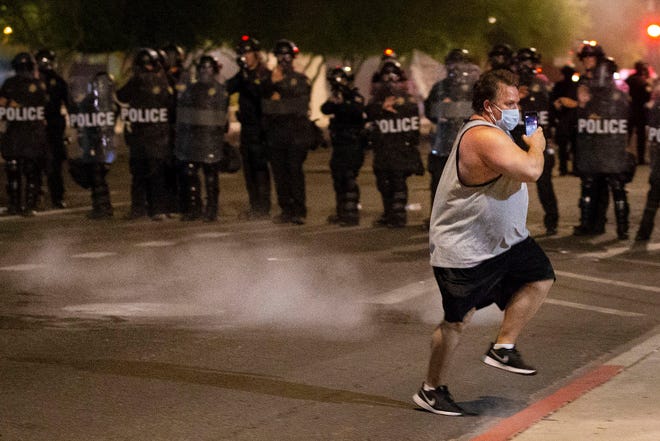 Phoenix Police officers in riot gear in riot gear fire pepper balls at a protester outside police headquarters during a rally in Phoenix on May 29, 2020, and march to remember Dion Johnson who was shot and killed during a struggle with a DPS trooper on May 25.