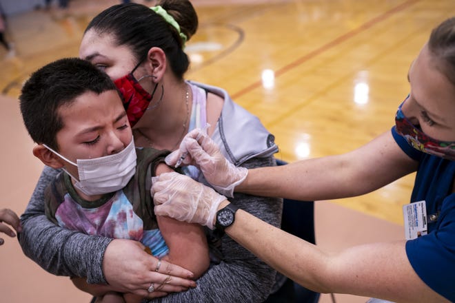 AJ Griego, 5, left, is administered his first dose of the COVID-19 vaccine by Merissa Doubleday, right, while his mother Veronica Griego, top left, holds him on Saturday, Nov. 6, 2021, at Carl Hayden Community High School in Phoenix.