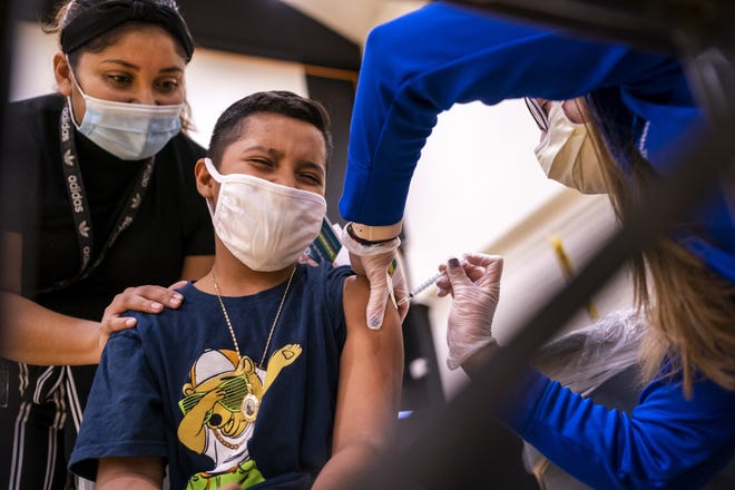 Anselmo Duran, 10, center, receives his first dose of the COVID-19 vaccine from Rebecca Weber, right, as his mother Francisca Ramirez, left, comforts him on Saturday, Nov. 6, 2021, at Maryvale High School in Phoenix.