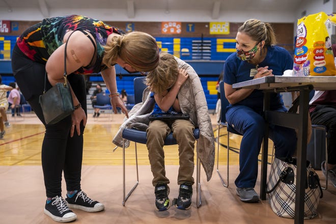 Taavi Rolland-Kieth, 7, center, is comforted by his mother Lisa, left, and Merissa Doubleday, right, before receiving his first dose of the COVID-19 vaccine on Saturday, Nov. 6, 2021, at Carl Hayden Community High School in Phoenix.