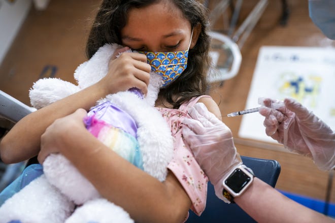 Ximena Tena, 8, receives her first dose of the COVID-19 vaccine while holding onto her stuffed unicorn on Saturday, Nov. 6, 2021, at Carl Hayden Community High School in Phoenix.