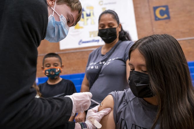 Estrella Garcia, 11, right, is administered her first dose of the COVID-19 vaccine by Ally Trovato, left, as her mother Gladys Garcia, center, watches on Saturday, Nov. 6, 2021, at Carl Hayden Community High School in Phoenix.