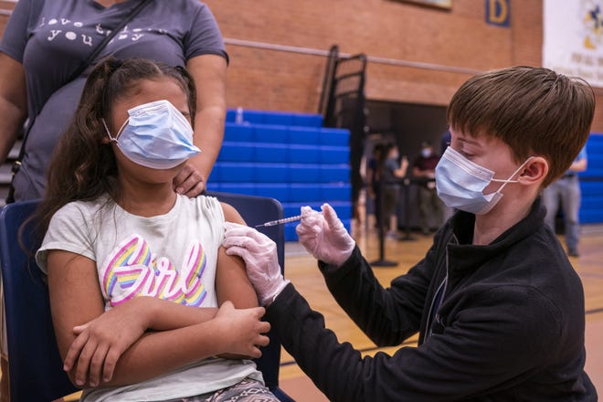 Rebeca Escalante, 8, of Mexico, left, puts her mask over her eyes as she's administered the COVID-19 vaccine by Ally Trovato, right, on Saturday, Nov. 6, 2021, at Carl Hayden Community High School in Phoenix.
