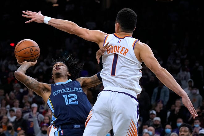 Memphis Grizzlies guard Ja Morant scores against Phoenix Suns guard Devin Booker (1) in the last second of an NBA basketball game Monday, Dec. 27, 2021, in Phoenix. The Grizzlies won 114-113.