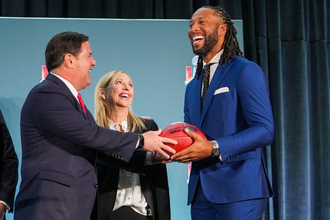 Doug Ducey, governor of Arizona, left, hands off a football to Larry Fitzgerald, former Cardinals wide receiver and executive chairperson of the Arizona Super Bowl host committee, right, as Jay Parry, Arizona Super Bowl Host Committee CEO, center, smiles during the official Super Bowl Host Committee handoff press conference at the Los Angeles Convention Center on Monday, Feb. 14, 2022, in Los Angeles.