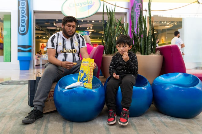 Juan Garcia (left) eats Wetzel ' s Pretzels with his stepson, Manuel Higuera, in a small seating area at Chandler Fashion Center on Feb. 20, 2022.