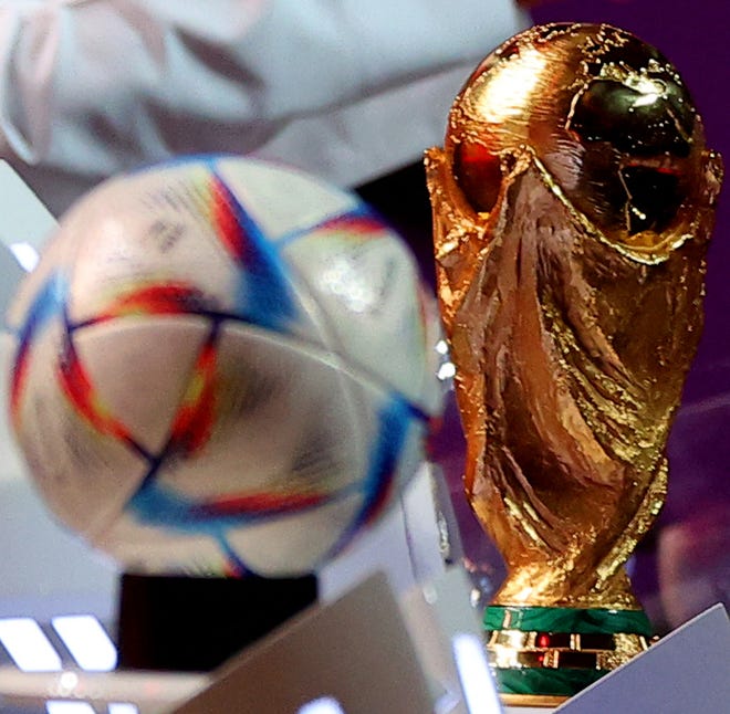 The official 2022 World Cup ball - called "Al-Rihla" - and the FIFA World Cup trophy are seen on stage during the draw in Qatar.