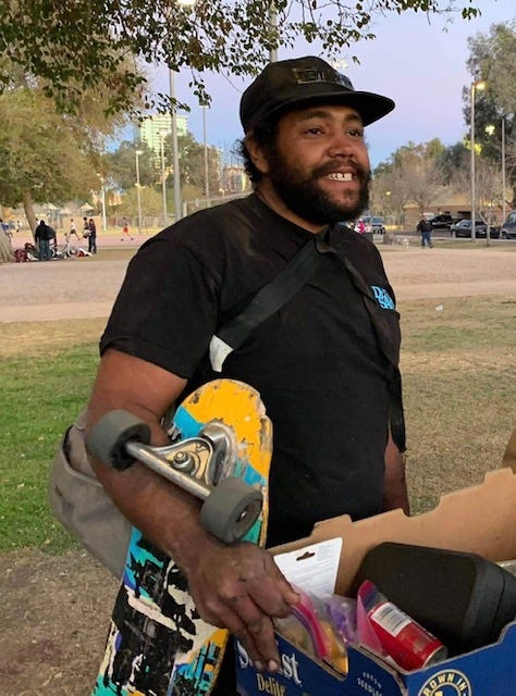 Sean Bickings, largely known as Madrocks in the Tempe community, stands holding a box and a skateboard at a park in an undated photo.