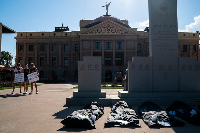 A group of protesters pose for a photo while an installation of body bags lays on the floor at the Arizona State Capitol during the annual March for Our Lives protest, a nationwide demonstration in support of gun control legislation, on Saturday, June 11, 2022.