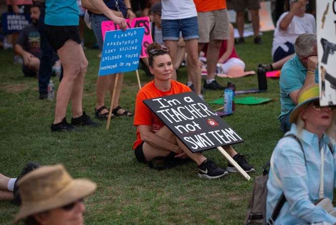 Sara Runyon (center) holds a sign rebuking calls to arm teachers as a solution to mass shootings in schools as hundreds of people gathered outside the Arizona Capitol on June 11, 2022, in Phoenix to demonstrate for stricter gun laws in response to recent mass shootings.