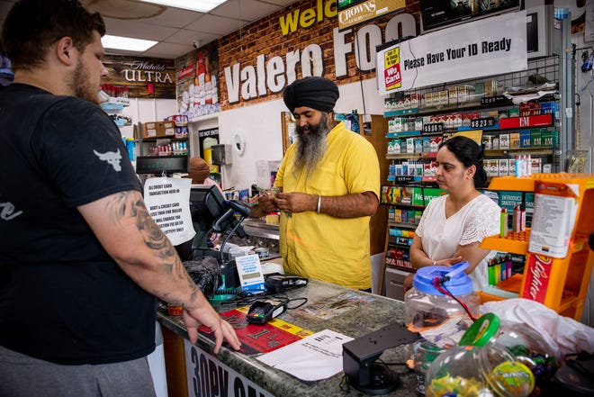 Jaswinder Singh with his wife Ramandeep Kaur, right, tend to a customer paying for gas inside their store at the corner of 20th Street and Osborn Road in Phoenix on June 21, 2022.