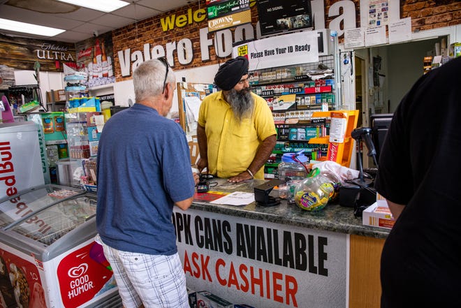 Jaswinder Singh, center, one of the owners of the pump station on the corner of 20th Street and Osborn Road in Phoenix, attends to a customer inside his store on June 21, 2022.